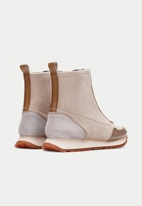 Botines de ante beige con detalles de cuero y paneles laterales elásticos. Cuentan con una suela de goma texturizada para mayor agarre y durabilidad.