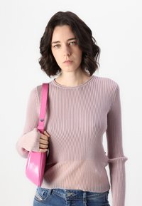 Lyserød ribbestrikket sweater med lange ærmer og flagrende manchetter, parret med en glansfuld lyserød håndtaske. Denim synlig ved midtsektionen.
