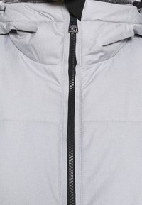 Gros plan sur une veste gris clair avec une fermeture éclair frontale noire et une capuche rembourrée dotée d'une doublure en tissu doux.