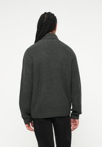 Mørkegrøn strikket sweater med en tekstureret overflade, et krave og ribbede manchetter. Sweateren har en løs pasform og falder til hoften.