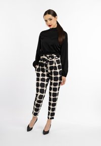 Zwarte satijnen blouse met lange mouwen, gecombineerd met hooggewaiste zwart-wit geruite broek. Model draagt puntige zwarte hakken.
