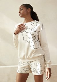 Lichtbeige sweatshirt met zwart bloemmotief, gecombineerd met bijpassende shorts met hetzelfde patroon. Zachte, gestructureerde stof.