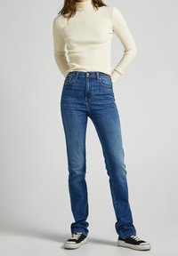 Hladký krémový rolák v proužkovaném vzoru spárovaný s tmavě modrými džíny. Tenisky mají černou textilii a bílé gumové podrážky. Čistý design, přiléhavý střih.