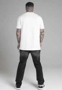 T-shirt bianco a maniche corte abbinato a jeans neri. Il tessuto appare morbido e la maglietta ha una vestibilità standard con orlo dritto.