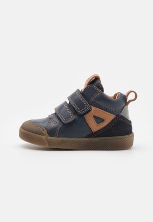 Bottines hautes en cuir bleu et suède avec des accents bruns, des bandes Velcro et une semelle en caoutchouc texturée. Conçues pour le confort et le soutien.
