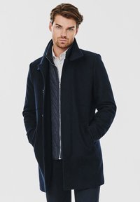 Granatowy płaszcz z wełny z domieszką, z wykładanym kołnierzem, przednimi kieszeniami i pikowaną podszewką. Materiał ma gładką fakturę i klasyczny krój.