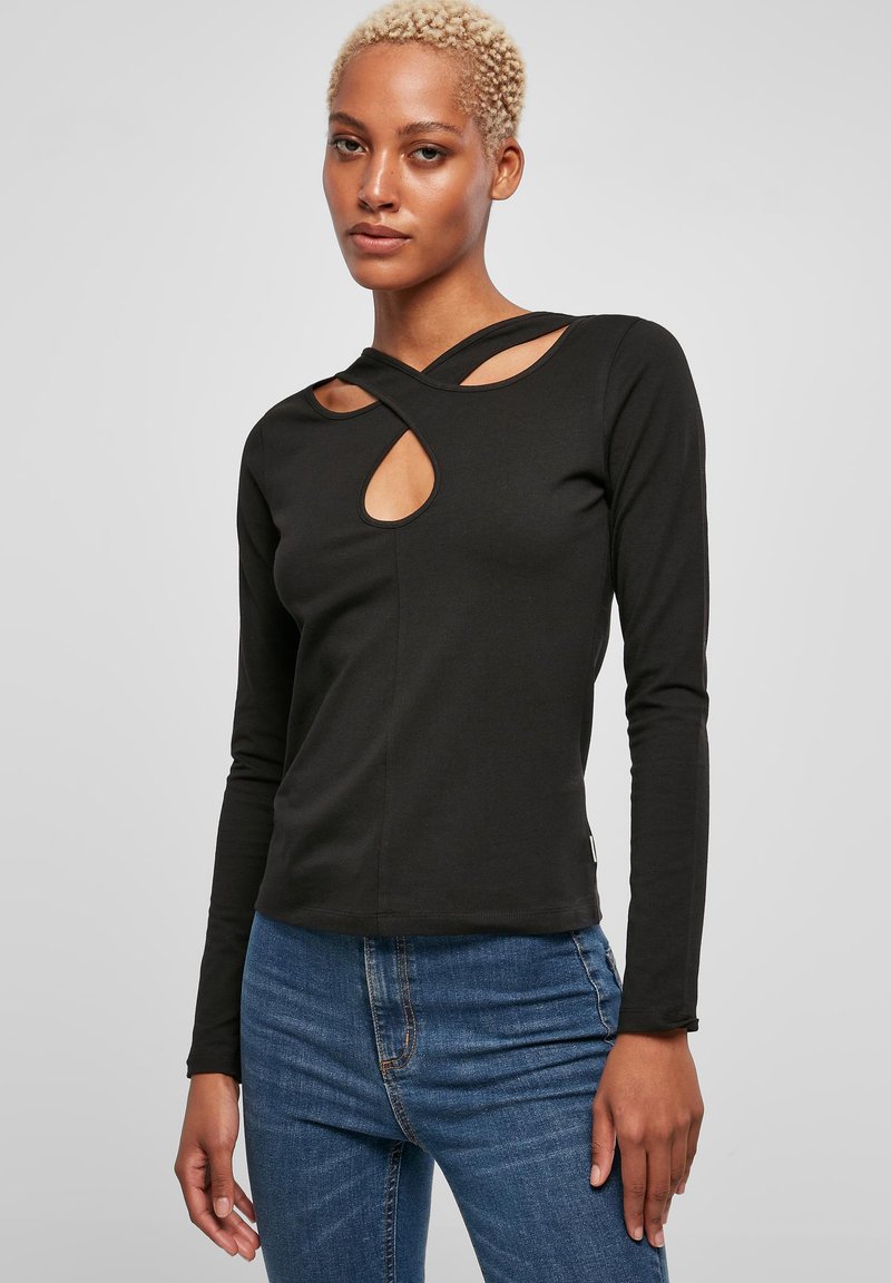 Schwarzes Langarmoberteil mit Cut-Out-Details, mit einem kreuzförmigen Ausschnitt und glatter Textur, kombiniert mit blauen enganliegenden Jeans.