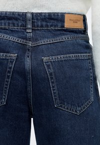 Σκούρο μπλε τζιν παντελόνια με ψηλή μέση, με αντιθετικές ραφές, δύο πίσω τσέπες και καφέ δερμάτινη ετικέτα μάρκας στη μέση.