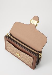 Brown leather handbag with a beige patterned front, gold hardware, and a flap closure. Interior features multiple compartments and a zipper.