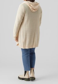 Helle beige Strickjacke mit Kapuze, lockere Passform, gerippter Saum, kombiniert mit blauen Jeans und beigen Ankle Boots mit dunklen Akzenten.