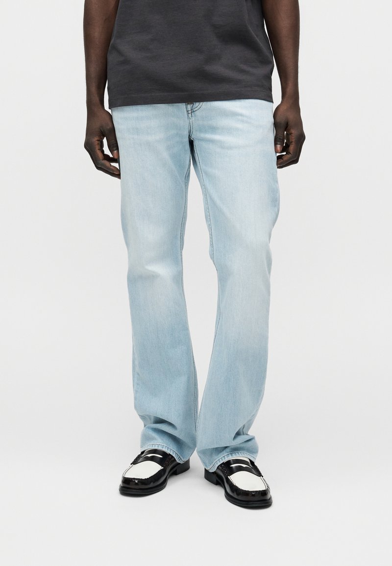 Φωτεινό γαλάζιο τζιν παντελόνι με ίσια γραμμή, με διακριτικά σημάδια συγκέντρωσης χρώματος και σε συνδυασμό με μαύρα και λευκά loafers.