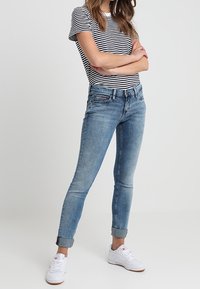 Vaqueros de mezclilla azul de corte slim, con un lavado desgastado y puños enrollados. Combinados con una camiseta de rayas en blanco y negro y zapatillas blancas.