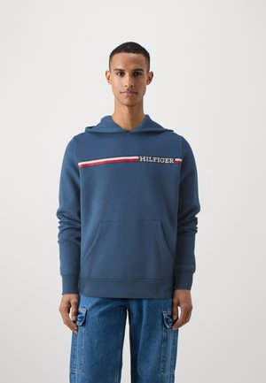 Kék pamut kapucnis felső, elülső zsebbel, bordázott mandzsettákkal, és egy vízszintes csíkkal, amelyen fehér "HILFIGER" felirat található.