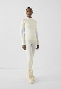 Top beige chiaro a maniche lunghe con maniche testurizzate, abbinato a leggings coordinati e stivaletti color crema. Design minimalista con motivi sottili.