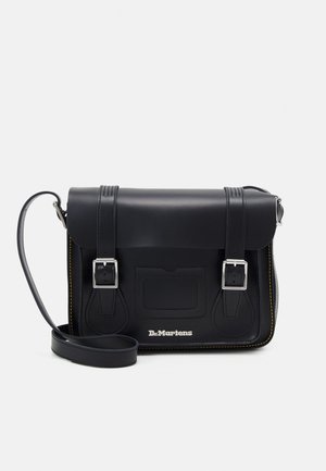 Sac cartable en cuir noir avec deux sangles à boucle, une bandoulière réglable, des surpiqûres jaunes et le logo Dr. Martens sur la poche avant.