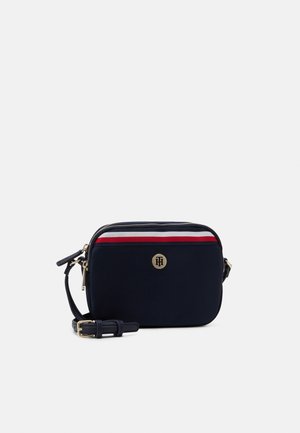 Marineblauwe crossbodytas met verstelbare schouderband, rood-wit gestreept detail bovenaan en een klein rond gouden logo aan de voorkant.