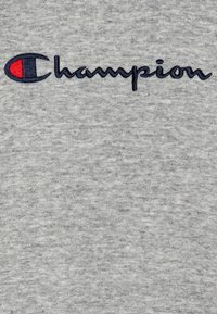 Tejido de algodón gris con una textura suave que presenta un logo bordado en náutica "Champion" y un pequeño acento rojo en la letra "C."