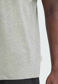 Camiseta de manga corta en gris claro, hecha de una suave mezcla de algodón. Presenta un dobladillo recto con una pequeña etiqueta en el lado izquierdo.