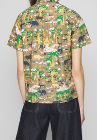 Košile s krátkým rukávem z bavlny s hnědým pozadím, která má po celé ploše barevné tiskoviny zvířat a přírody. Uvolněný střih a zapínací límec.