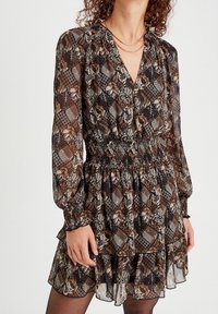 Robe à motifs noirs et bruns avec des manches longues, une taille smockée et un ourlet en couches de volants. Tissu transparent avec des motifs floraux et géométriques.