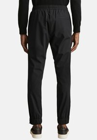 Pantaloni de jogging negri cu talie elastică, croială ajustată și tivuri strânse. Prezintă un singur buzunar pe spate și o textură a materialului neted.