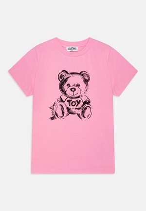 Różowa koszulka z krótkim rękawem wykonana z miękkiej tkaniny, zdobiona grafiką czarnego niedźwiedzia z napisem "ZABAWKA" na koszulce. Prosty dekolt w serek.