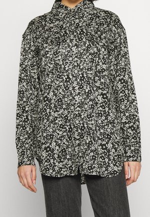 Langärmeliges Hemd zum Knöpfen in Schwarz mit weißem Blumenmuster. Mit Kragen und lockerer Passform. Der Stoff wirkt seidig mit glatter Textur.