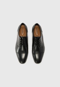 Zapatos de vestir de cuero negro con punta afilada, diseño de cordones y forro interior en tono marrón. Textura suave con sutiles detalles de costura.