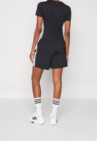 T-shirt de sport noir et short avec des rayures blanches sur les côtés, associés à des chaussures blanches et des chaussettes rayées. Tissu lisse, design ajusté.