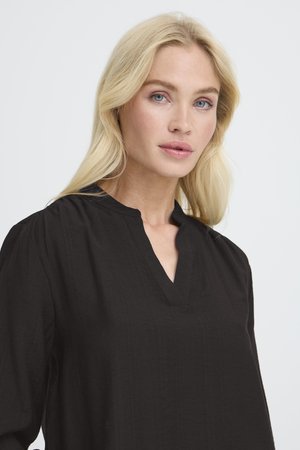 Zwarte, lichte blouse met een gespleten halslijn en lange mouwen. De stof heeft een gestructureerde afwerking, wat zorgt voor een zachte uitstraling.