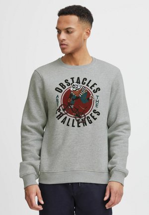 Sweatshirt gris clair avec un col rond. Présente un design graphique d'un panda à vélo, entouré du texte "Les obstacles sont des défis."