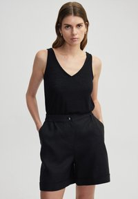 Zwarte mouwloze top met een V-hals, gecombineerd met hoge zwarte shorts met een knoopsluiting en zijzakken, met een gladde textuur.