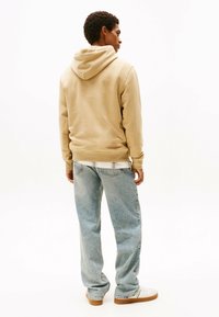 Beige hættetrøje med en afslappet pasform, kombineret med lyseblå denimjeans. Stoffet ser blødt ud med en glat overflade.