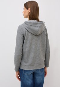 Grau kapuzenpullover mit strukturierter Oberfläche, mit abgerundetem Saum und Kängurutasche, kombiniert mit blauen Jeans.