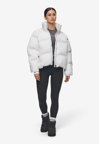 Vit puffjacka, fyrkantig design med hög hals. Bärs över en mörk topp och svarta leggar. Modell i svarta puffskor och mönstrade strumpor.