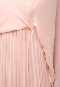 Mekana ružičasta plisirana tkanina skupljena na ušivenom šavu s glatkim naboranim slojem koji stvara slojevitu teksturu.