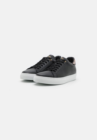 Black leather sneakers with white rubber soles, round laces, gold eyelets, and a striped accent on the heel. Smooth texture throughout.