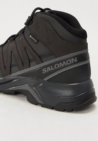 Czarne buty trekkingowe z teksturowanym cholewką, wzmocnionym palcem i szarymi akcentami; zawiera etykietę GORE-TEX oraz zaawansowaną technologię podwozia.