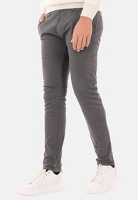 Pantaloni di cotone grigi con vestibilità slim e una leggera lucentezza, con una parte anteriore piatta, tasche laterali, abbinati a sneakers bianche.