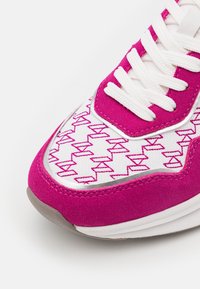 Sneakers med en överdel i rosa mocka och vit tyg. Har intrikata rosa geometriska sömmar, vita snören och en grå gummisula.