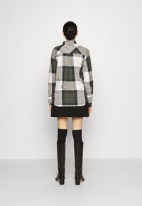 Koszula w kratę w odcieniach zieleni, granatu, bieli i szarości, z kołnierzykiem i mankietami na guziki, w połączeniu z czarną spódnicą i wysokimi czarnymi botkami.