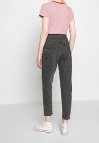 Jeans negros ajustados con cintura alta y dos bolsillos traseros, combinados con una camiseta de rayas rojas y blancas y zapatillas blancas.