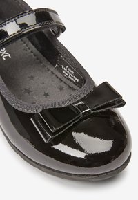 Schwarzer Lacklederschuh mit runder Zehenform, Satin-Schleifendetail an der Vorderseite und einem schwarzen elastischen Riemen. Das Innere hat einen Sternenprint.