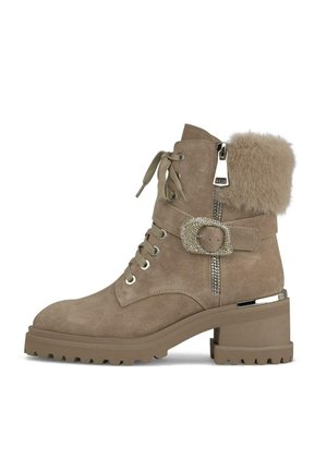 Bottines en suède taupe avec un soufflet en fourrure, un talon épais, des lacets à l'avant, une boucle décorative et une fermeture éclair sur le côté. Semelle en caoutchouc texturé.