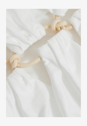 Biely textil s nariasenou textúrou, spojený svetlo béžovým lanom. Dizajn má jemné, plynulé tvary a uzlový akcent.