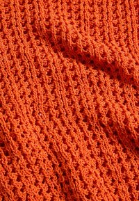 Gebreide textiel in fel oranje met een gestructureerd, open weefpatroon en opvallende, gedraaide garenkringdetails. Lichtgewicht en ademend.