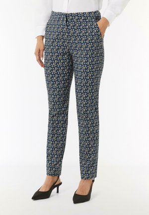 Pantalons bleu et beige à motifs en tissu tissé, design ajusté, avec poches et fermeture éclair à la cheville. Associés à des talons noirs.