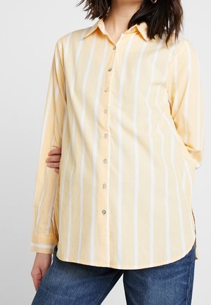 Camicia a maniche lunghe gialla a righe verticali con chiusura a bottoni, colletto e spacchi laterali. Il tessuto è strutturato con righe bianche verticali.
