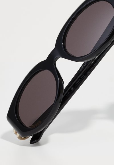 Occhiali da sole neri oversize con lenti arrotondate, caratterizzati da una finitura lucida e dettagli in metallo dorato. Made in Japan.