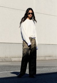 Krém színű, túlméretezett pulóver bordás textúrával, laza leopárdmintás nadrággal párosítva. Fekete napszemüveg és lapos fekete cipő egészíti ki a megjelenést.